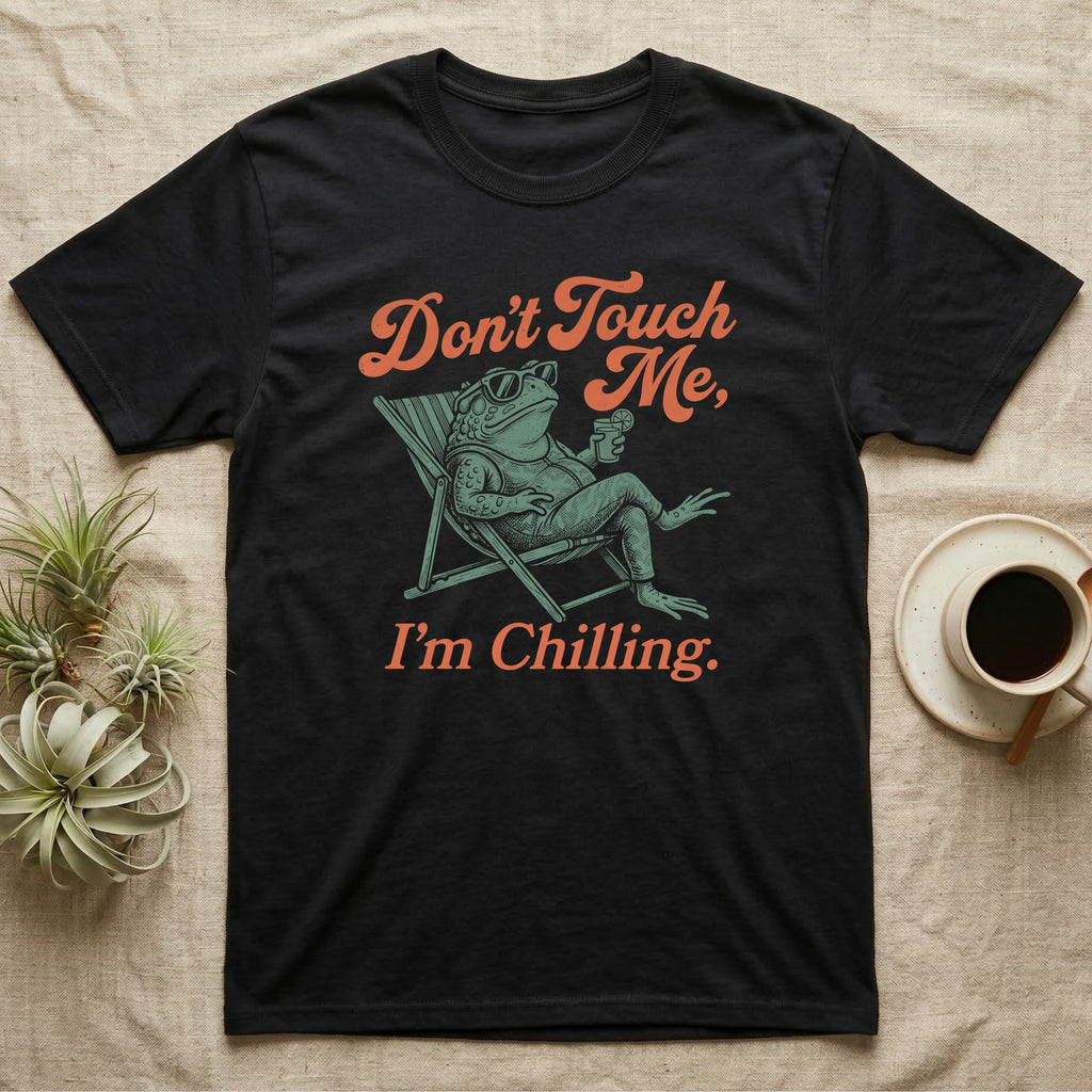 American Toad Deck Chair T-Shirt in Black — Illustrated American toad reclining in a deck chair with sunglasses and a drink, coral script reading Don't Touch Me I'm Chilling.