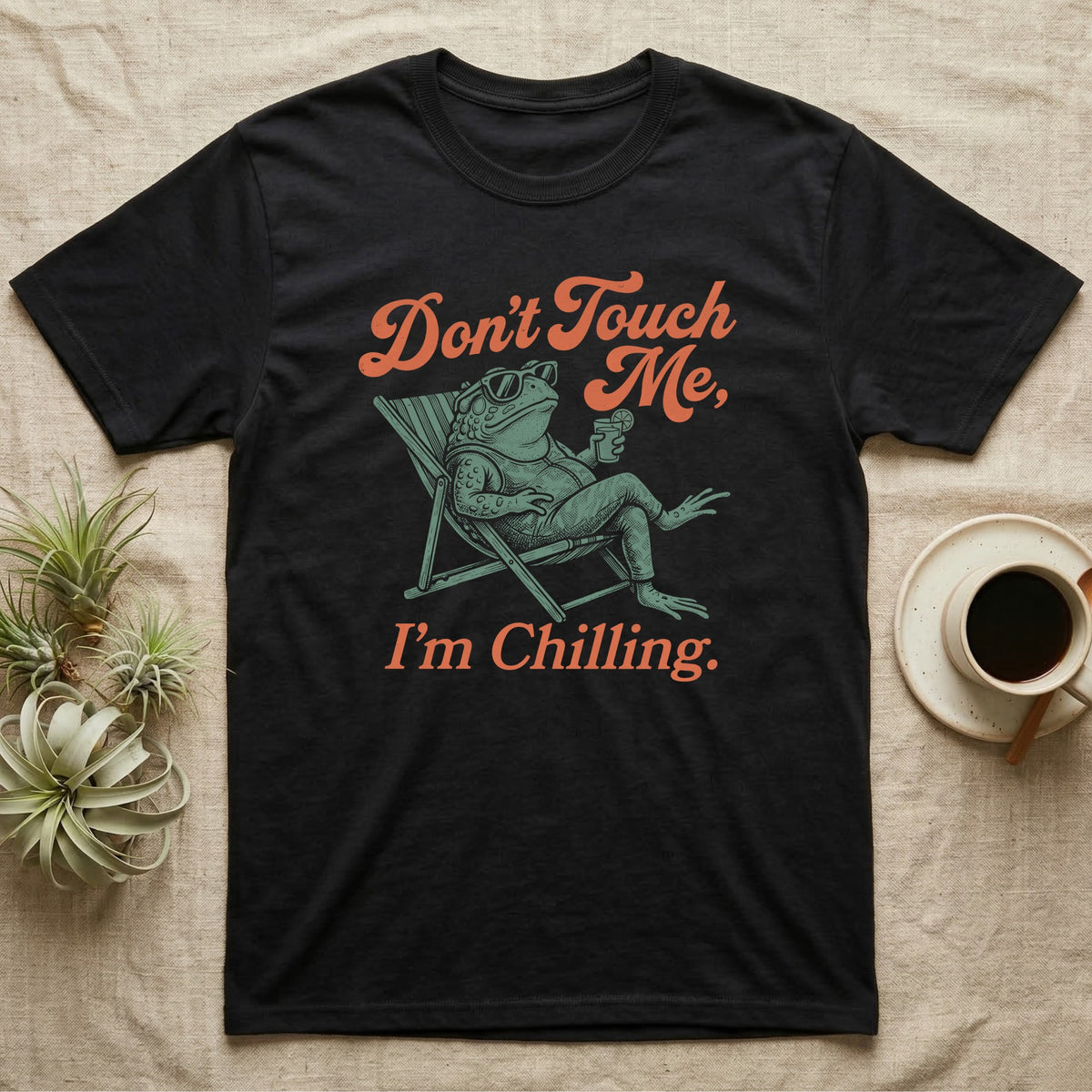 American Toad Deck Chair T-Shirt in Black — Illustrated American toad reclining in a deck chair with sunglasses and a drink, coral script reading Don't Touch Me I'm Chilling.