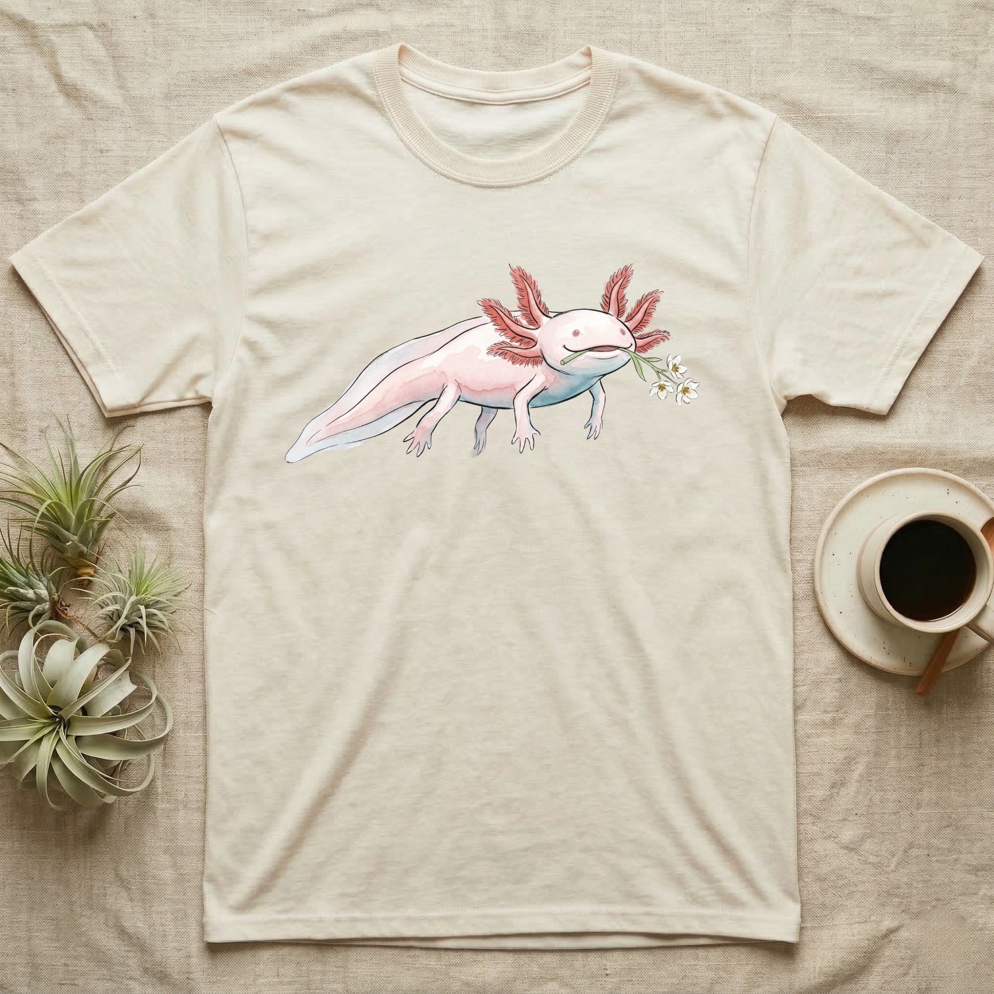 Axolotl Blossom T-Shirt in Natural — Watercolor illustration of a pink leucistic axolotl with feathery gills holding an aquatic blossom sprig, on a dark grey t-shirt.