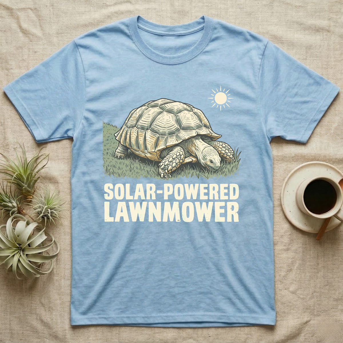 Solar Powered Lawnmower T-Shirt in Light Blue — Retro-illustration of a sulcata tortoise grazing a lawn stripe under a sun motif with a Solar-Powered Lawnmower caption.