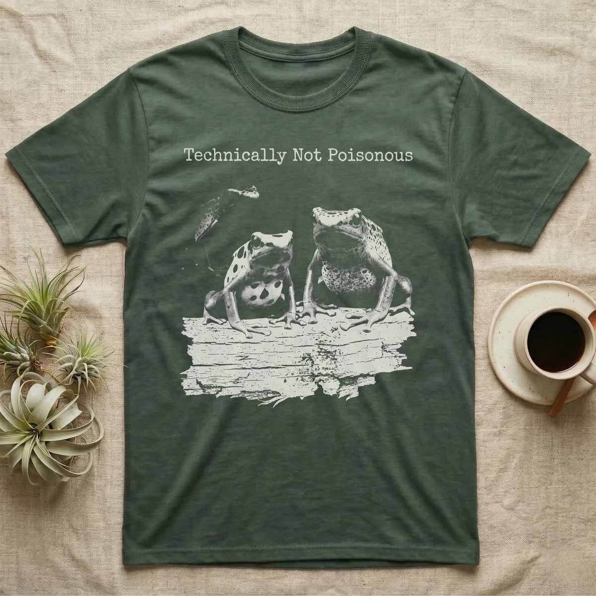 Technically Not Poisonous Dart Frog T-Shirt in Military Green — Three blue poison dart frogs on a bark ledge in distressed screen-print style under the line Technically Not Poisonous.