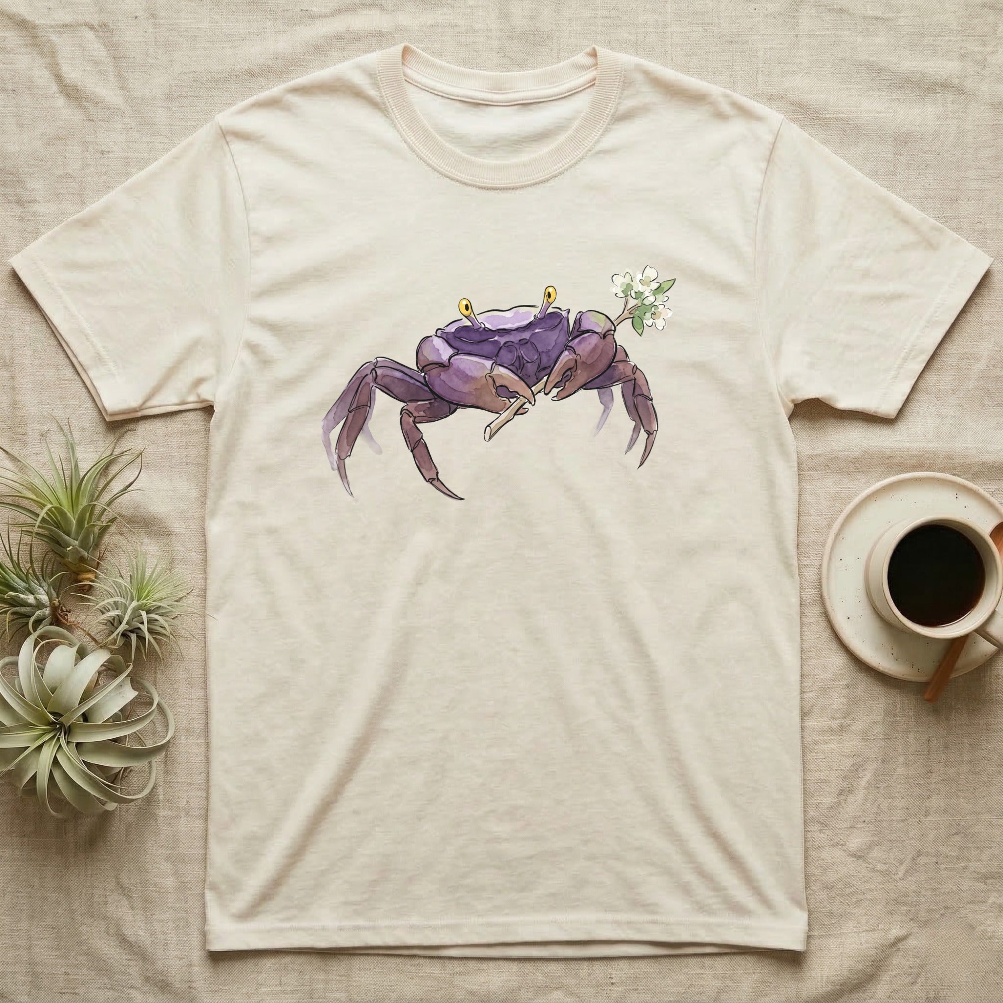 Vampire Crab Blossom T-Shirt in Natural — Watercolor illustration of a violet-purple vampire crab with yellow eye stalks holding a moss-flower blossom sprig, on a dark grey t-shirt.
