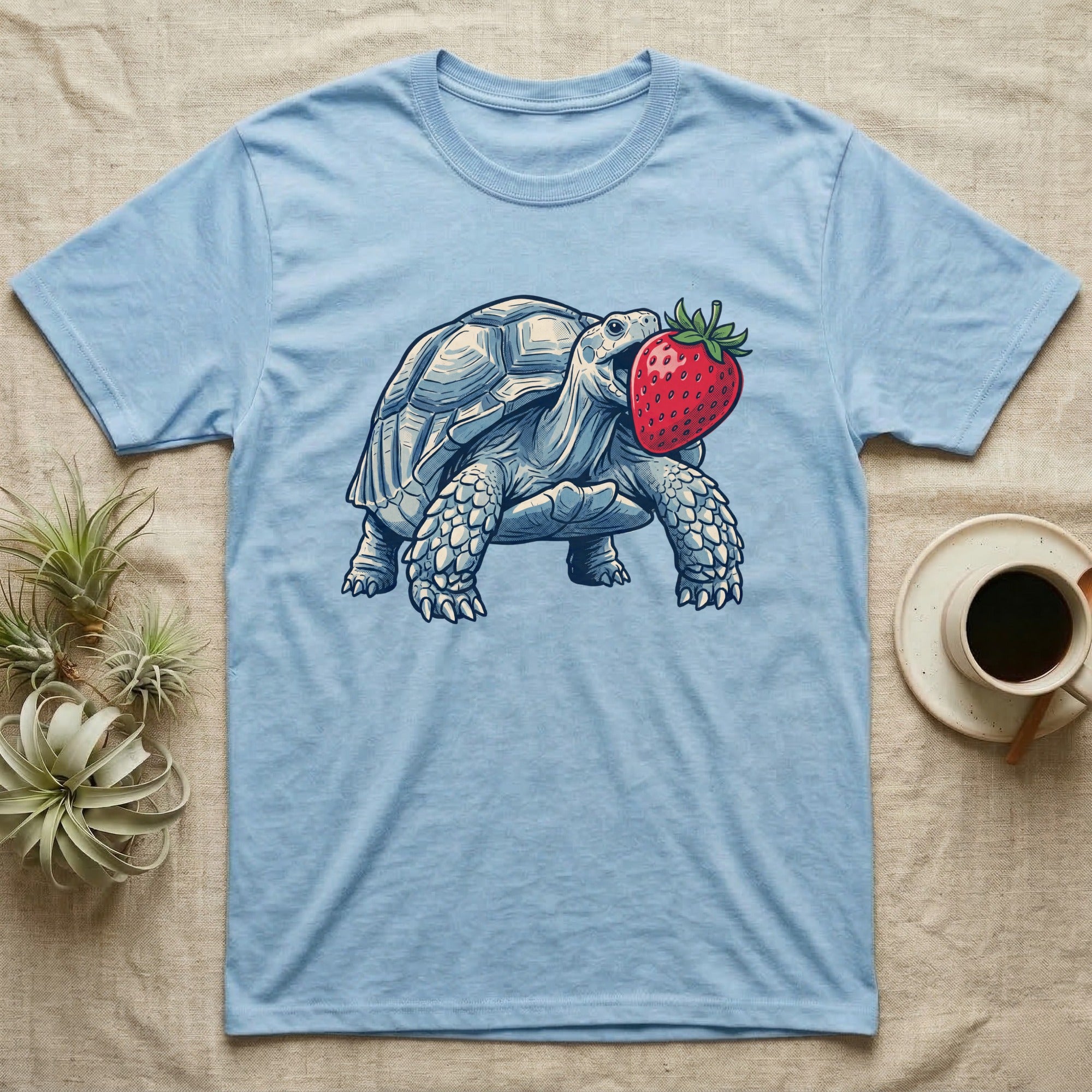 Sulcata Strawberry Tortoise T-Shirt in Light Blue — Bold vector illustration of a sulcata tortoise lunging neck-first toward an oversized red strawberry, head-on view.