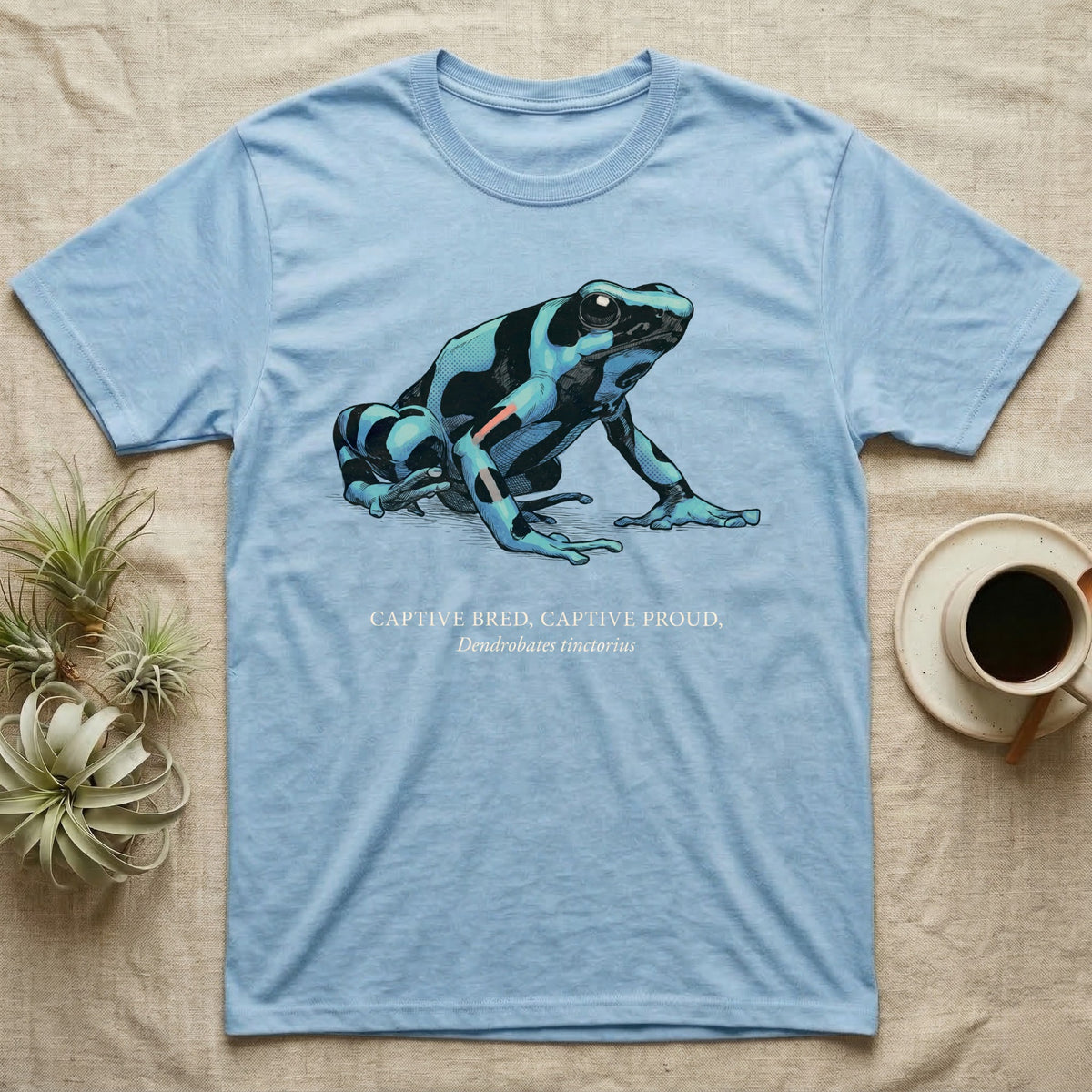 Captive Bred Frog T-Shirt in Light Blue — Naturalist-plate illustration of a healthy dyeing dart frog above a serif creed reading Captive Bred Captive Proud.