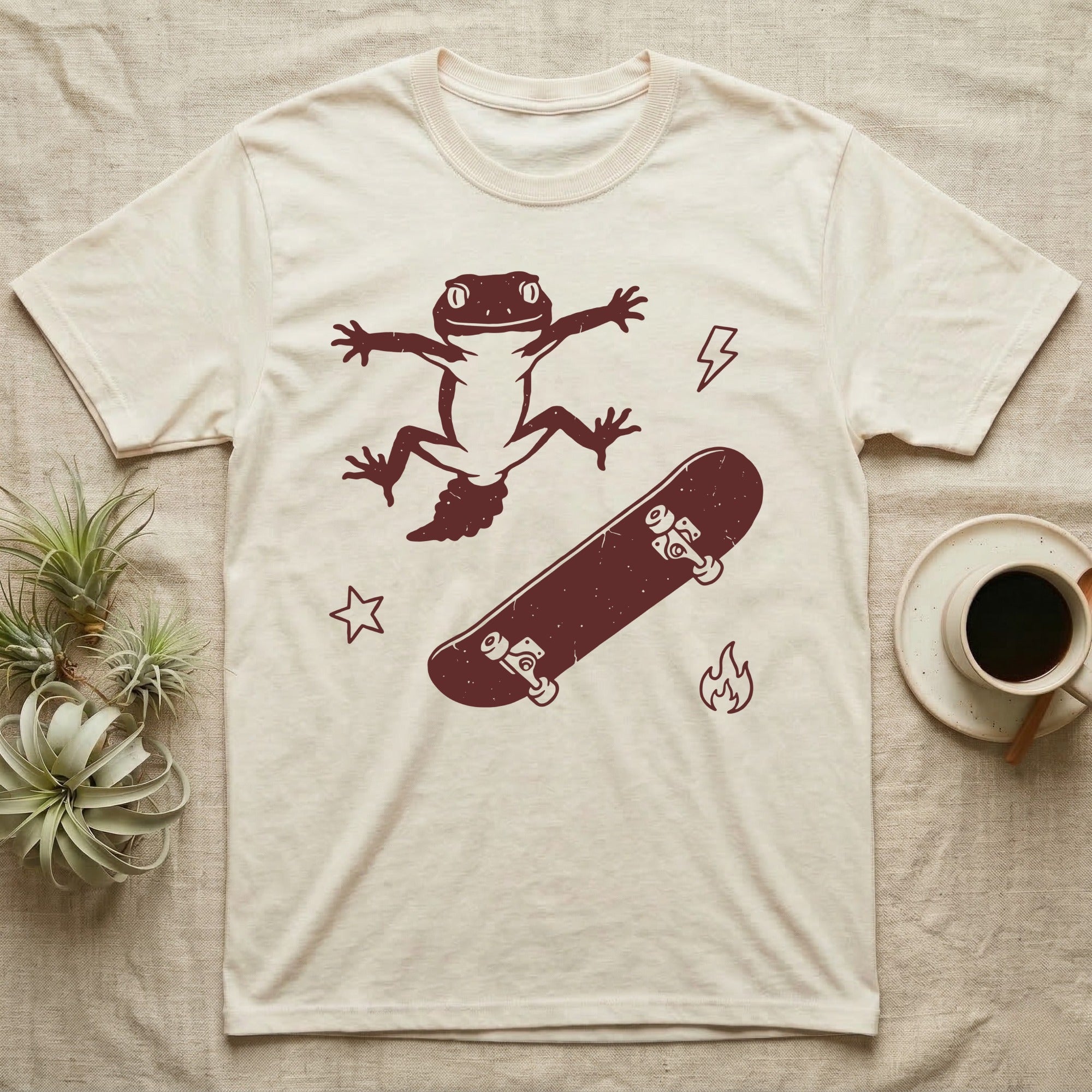 Knob-Tailed Gecko Kickflip T-Shirt in Natural — Distressed one-ink illustration of a knob-tailed gecko airborne mid-kickflip above a tumbling skateboard.