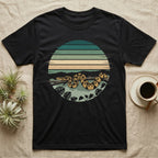 Ball Python Monstera T-Shirt in Black — Ball python coiled through a striped rainforest circle window with monstera and pothos on a near-black tee
