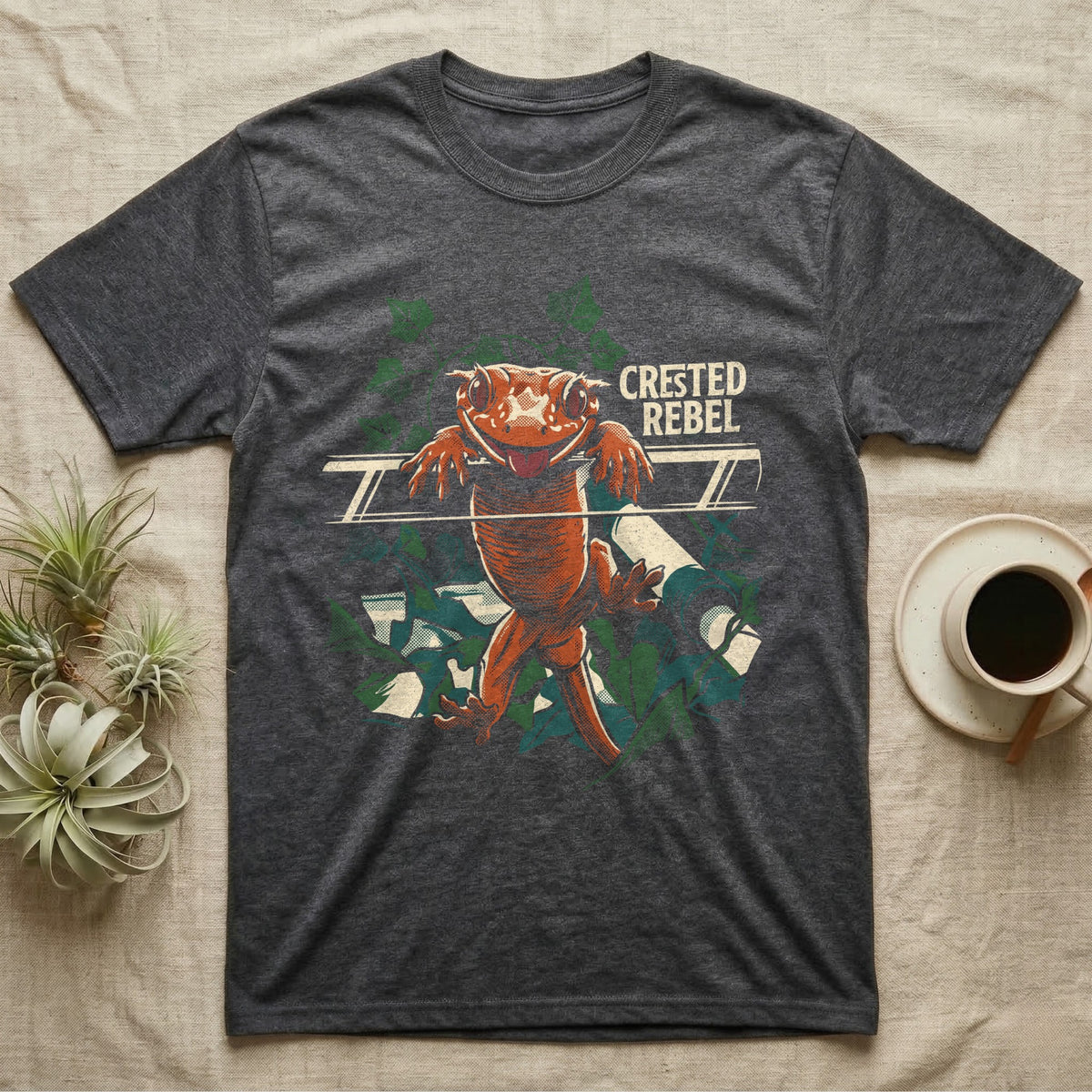 Illustration of a crested gecko hanging tongue-out over a rail among ivy leaves, bold distressed lettering reading Crested Rebel. — shown on a Dark Heather tee.