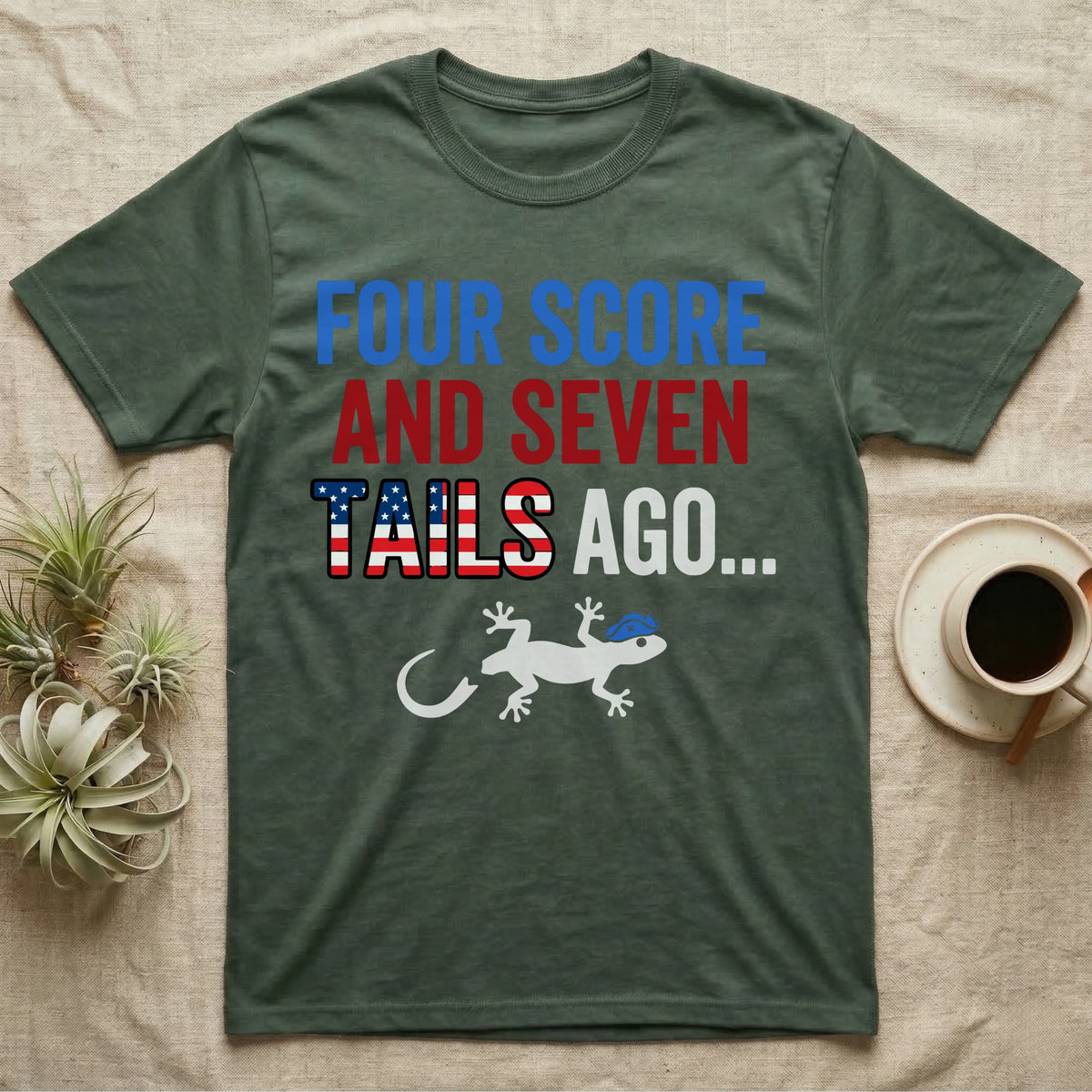 Gecko Four Score T-Shirt in Military Green — Block text Four Score and Seven Tails Ago with a flag-filled word above a white gecko silhouette shedding its tail.