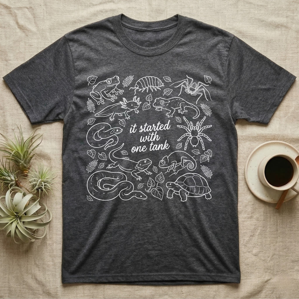Terrarium Keeper One Tank T-Shirt in Dark Heather — White outline illustration of eleven terrarium species — bearded dragon, crested gecko, ball python, axolotl, tortoise, tarantula, isopod, whip spider, chameleon, tree frog and hognose — with pothos and fern leaves, ringed around the script line it started with one tank.