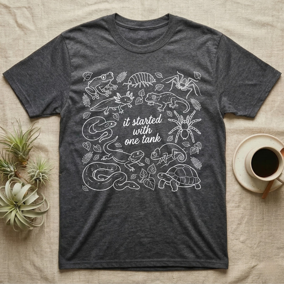 Terrarium Keeper One Tank T-Shirt in Dark Heather — White outline illustration of eleven terrarium species — bearded dragon, crested gecko, ball python, axolotl, tortoise, tarantula, isopod, whip spider, chameleon, tree frog and hognose — with pothos and fern leaves, ringed around the script line it started with one tank.