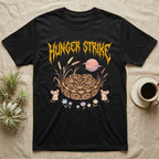 Ball Python Feral T-Shirt in Black — Ball python coiled in a loaf in a pastel savanna scene under a spiky honey-gold metal wordmark reading HUNGER STRIKE.