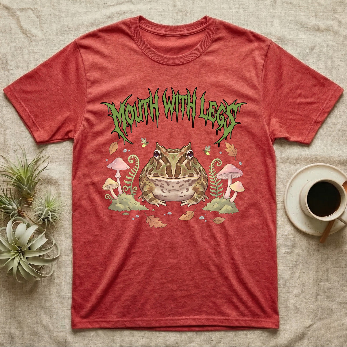 Pacman Frog Feral T-Shirt in Heather Red — Round Pacman frog in a pastel forest-floor scene under a spiky leaf-green metal wordmark reading MOUTH WITH LEGS.