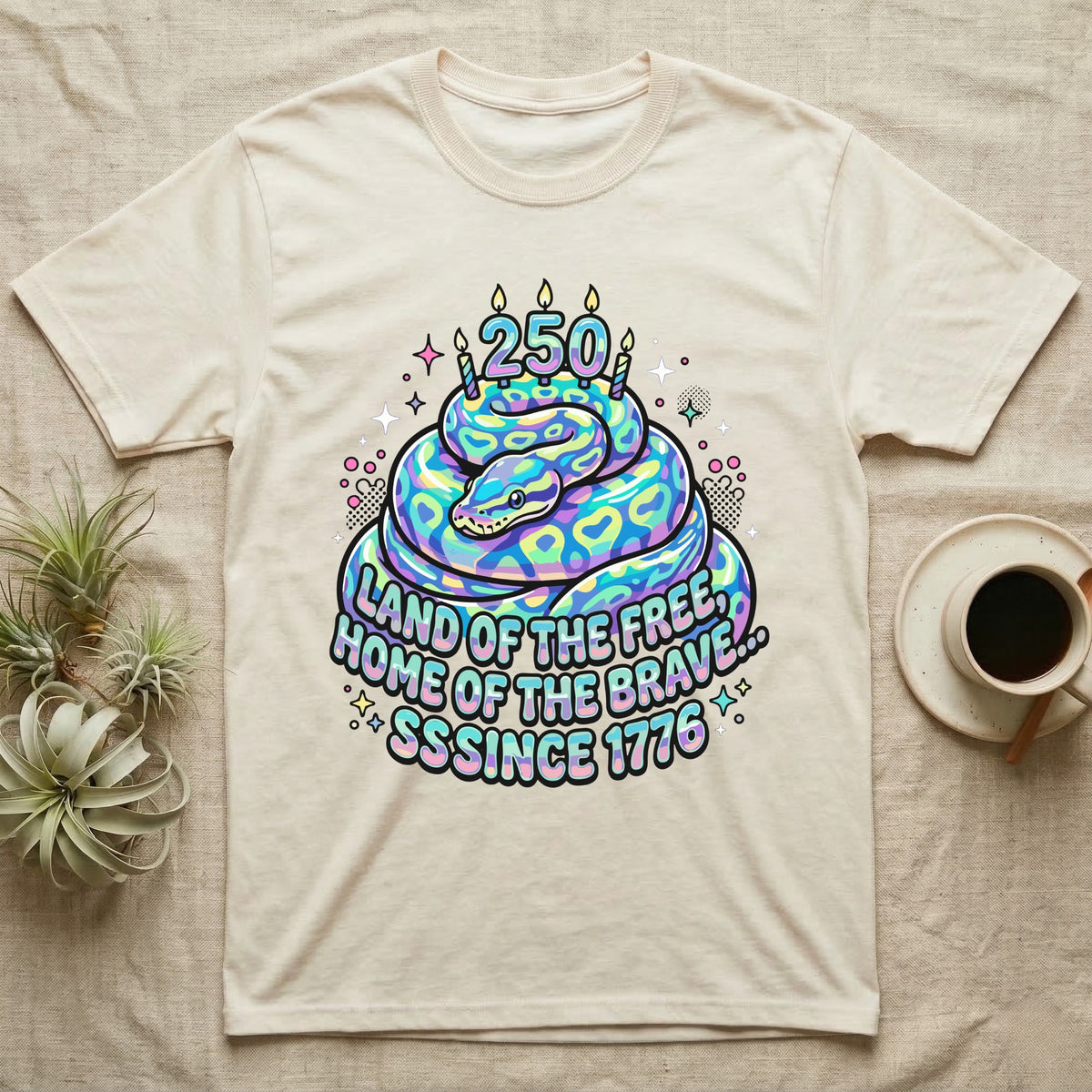 Ball Python Birthday Cake T-Shirt in Natural — Y2K pastel ball python coiled as a birthday cake with 250 candles and bubble text Land of the Free, Sssince 1776.