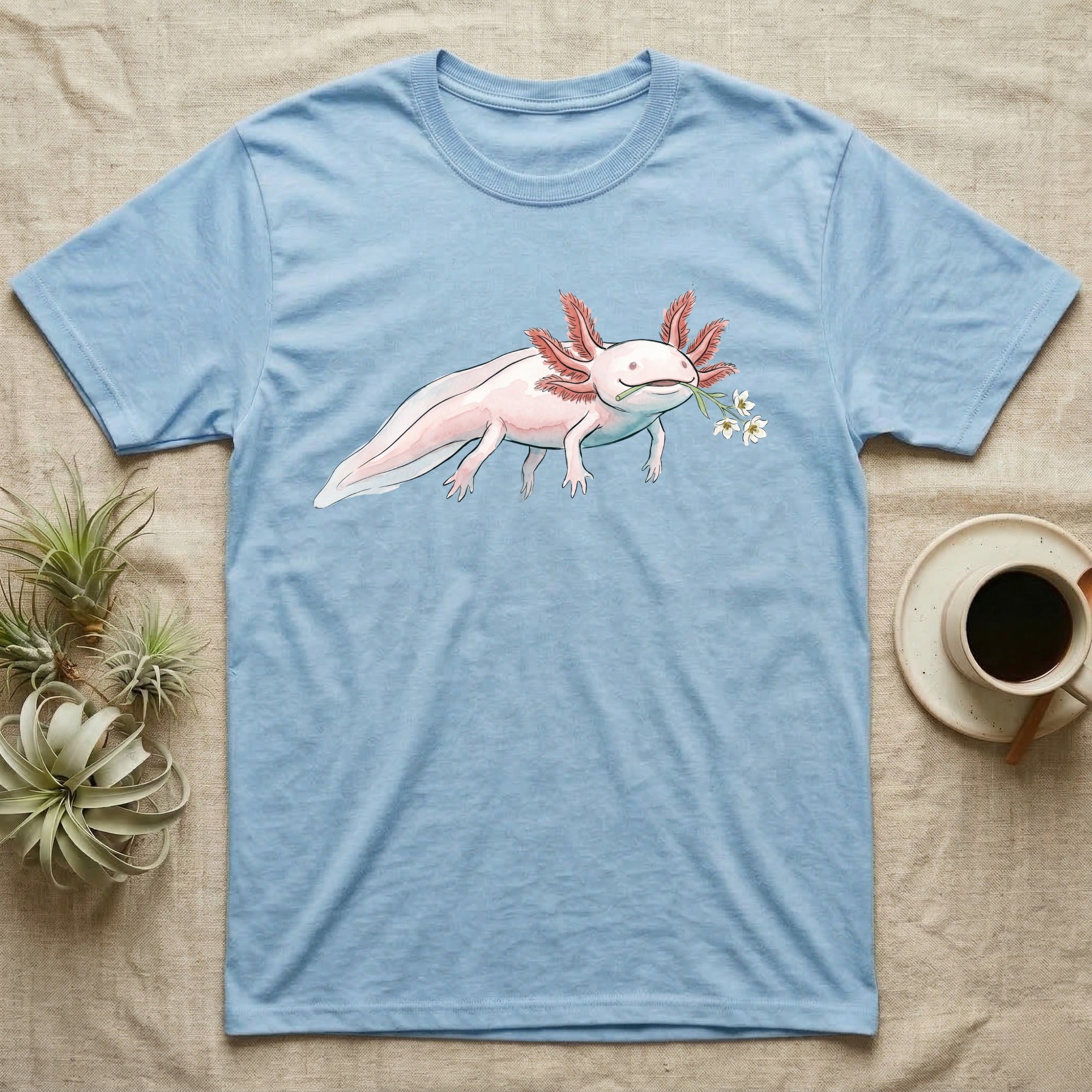 Axolotl Blossom T-Shirt in Light Blue — Watercolor illustration of a pink leucistic axolotl with feathery gills holding an aquatic blossom sprig, on a dark grey t-shirt.