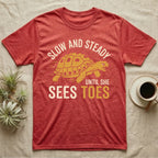 Hermann's Tortoise Toes T-Shirt in Heather Red — Golden ochre Hermann's tortoise charging to the right under arched cream words Slow And Steady, with Until She Sees Toes below