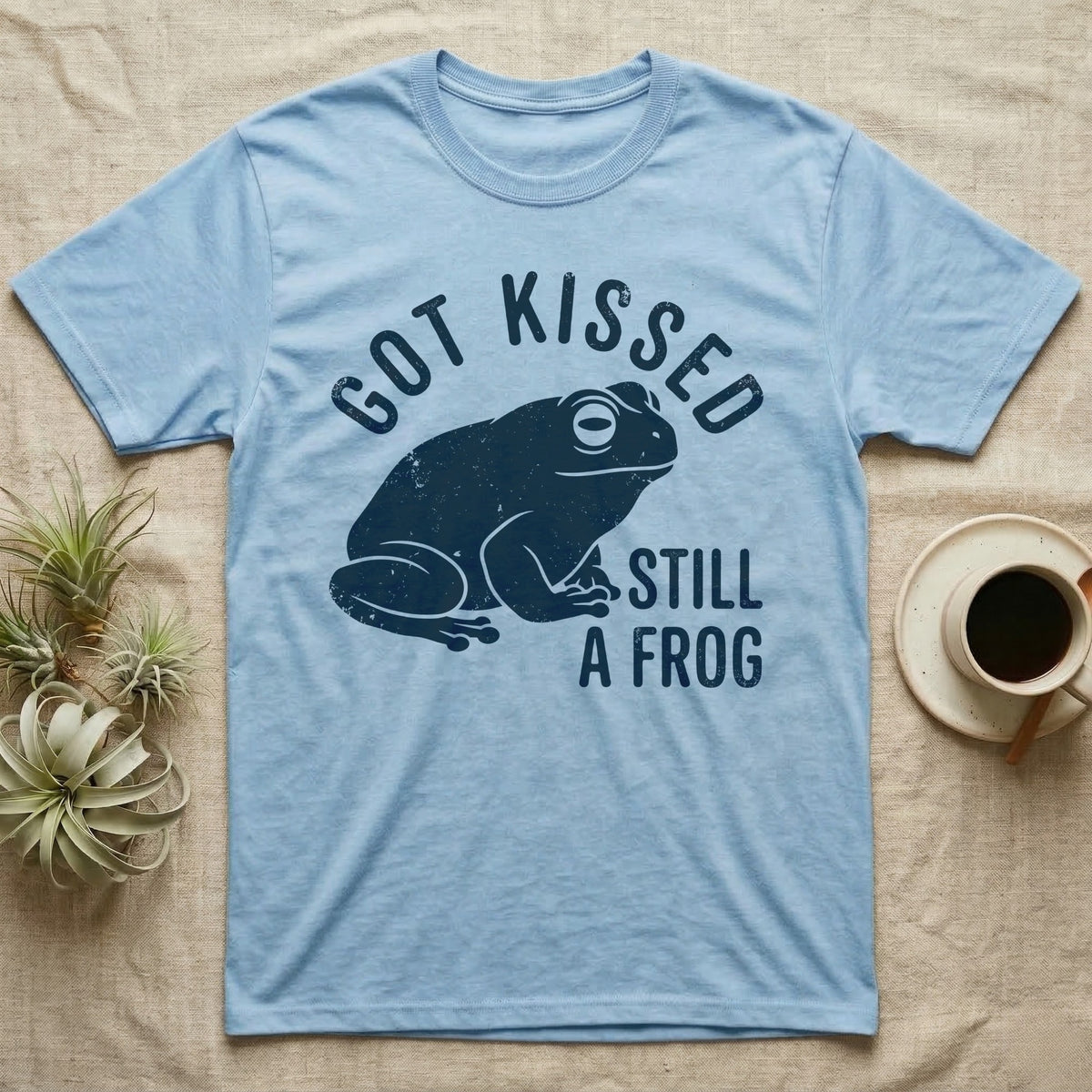 Tree Frog Kissed T-Shirt in Light Blue — Worn navy silhouette of a dumpy White's tree frog under the words Got Kissed Still A Frog