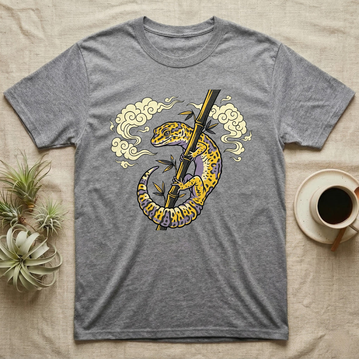Gray t-shirt with a yellow and purple leopard gecko on bamboo, surrounded by clouds.