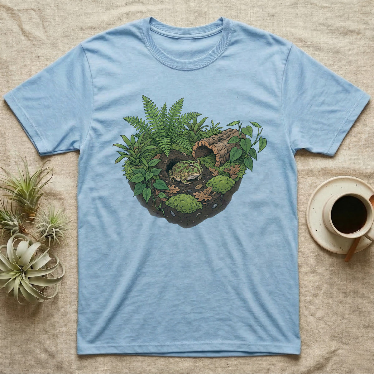 Pacman Frog Vivarium T-Shirt in Light Blue — Botanical illustration of a pacman frog thriving in a planted bioactive vivarium beside a small empty plastic cup.