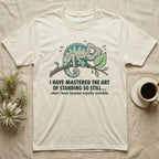 Cream t-shirt with a surprised chameleon on a branch and humorous text about invisibility.