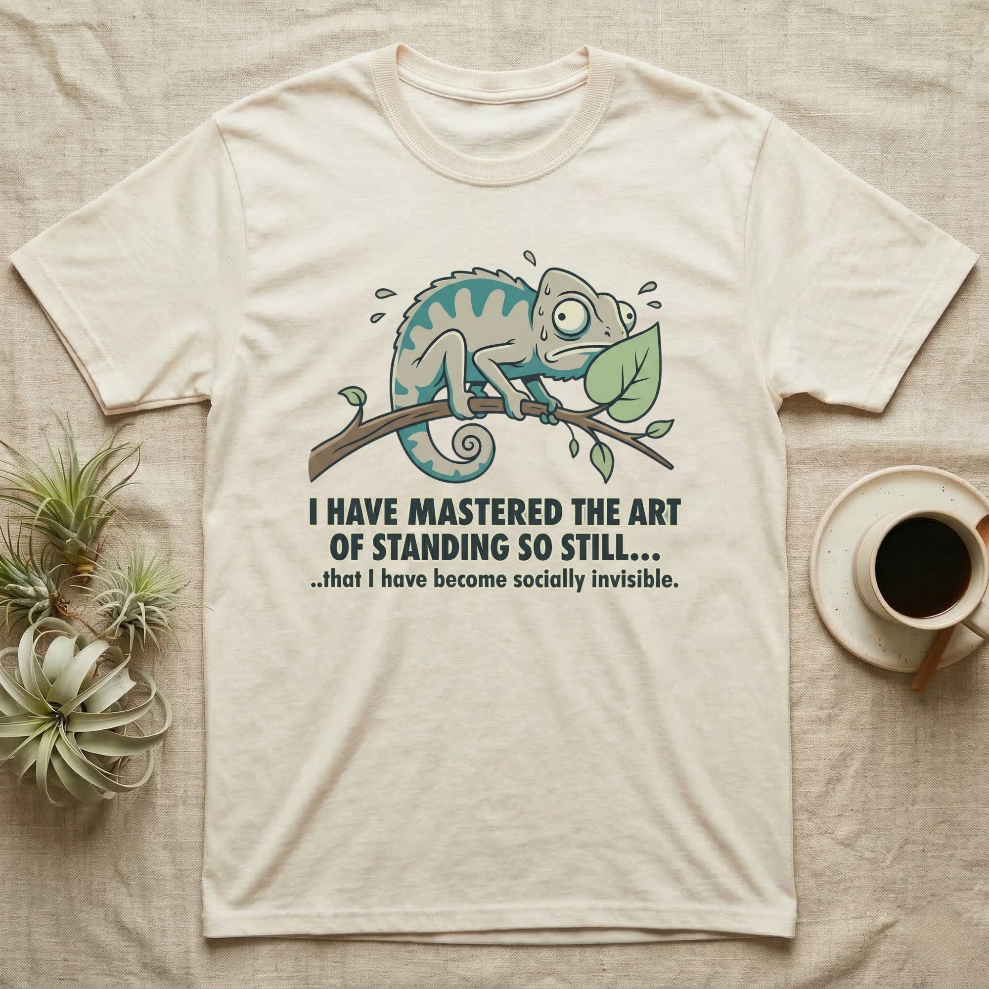 Cream t-shirt with a surprised chameleon on a branch and humorous text about invisibility.