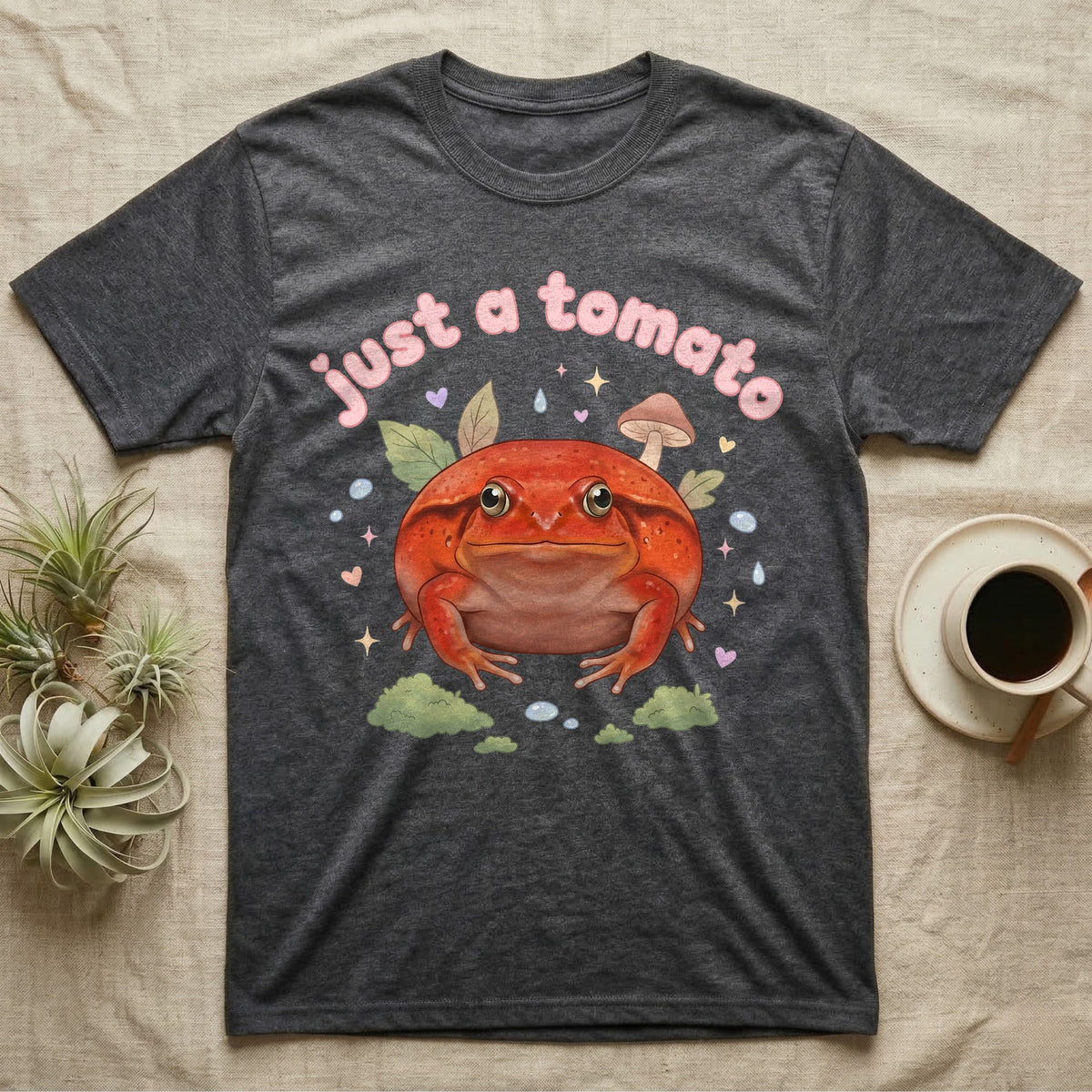 Tomato Frog Softie T-Shirt in Dark Heather — Round red-orange tomato frog facing forward under a puffy pastel "just a tomato" bubble wordmark with tiny hearts.