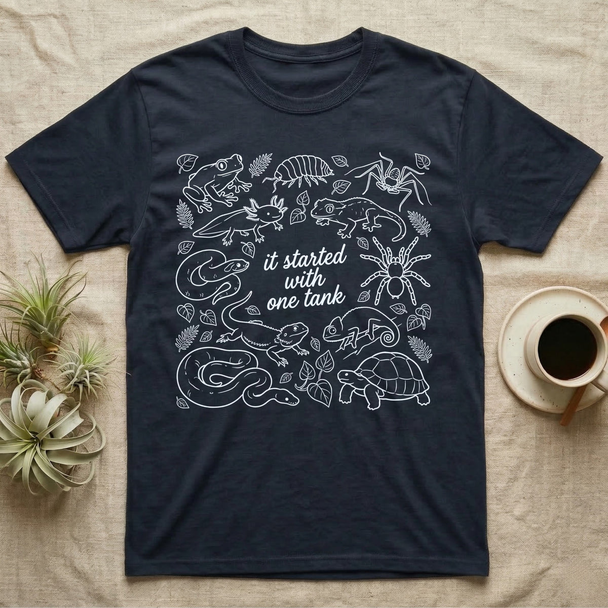 Terrarium Keeper One Tank T-Shirt in Navy — White outline illustration of eleven terrarium species — bearded dragon, crested gecko, ball python, axolotl, tortoise, tarantula, isopod, whip spider, chameleon, tree frog and hognose — with pothos and fern leaves, ringed around the script line it started with one tank.