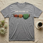 Green Tree Python Glow-Up T-Shirt in Sport Grey — Impasto illustration of a green tree python at three life stages on one branch: red hatchling, orange-brown subadult, green adult.
