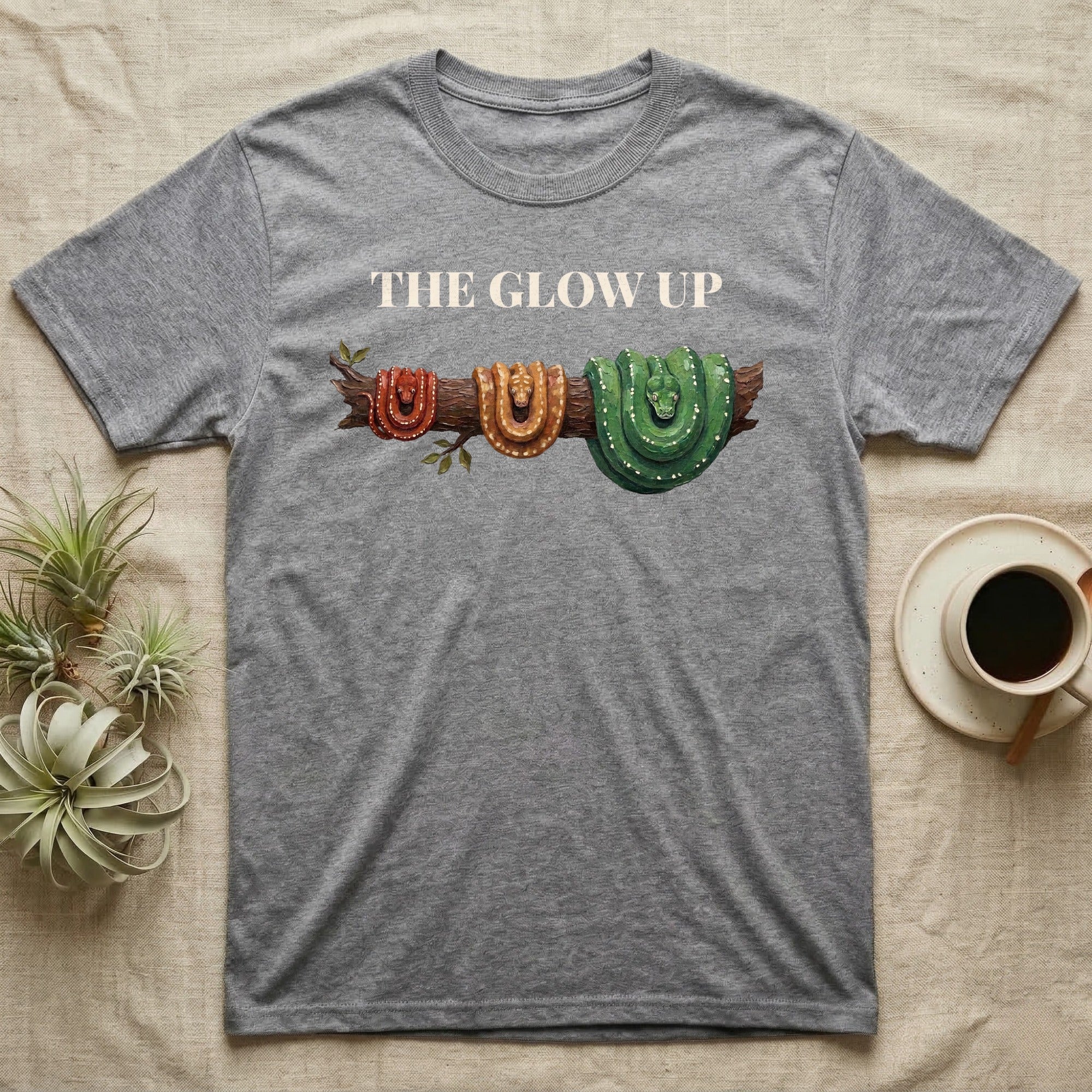 Green Tree Python Glow-Up T-Shirt in Sport Grey — Impasto illustration of a green tree python at three life stages on one branch: red hatchling, orange-brown subadult, green adult.