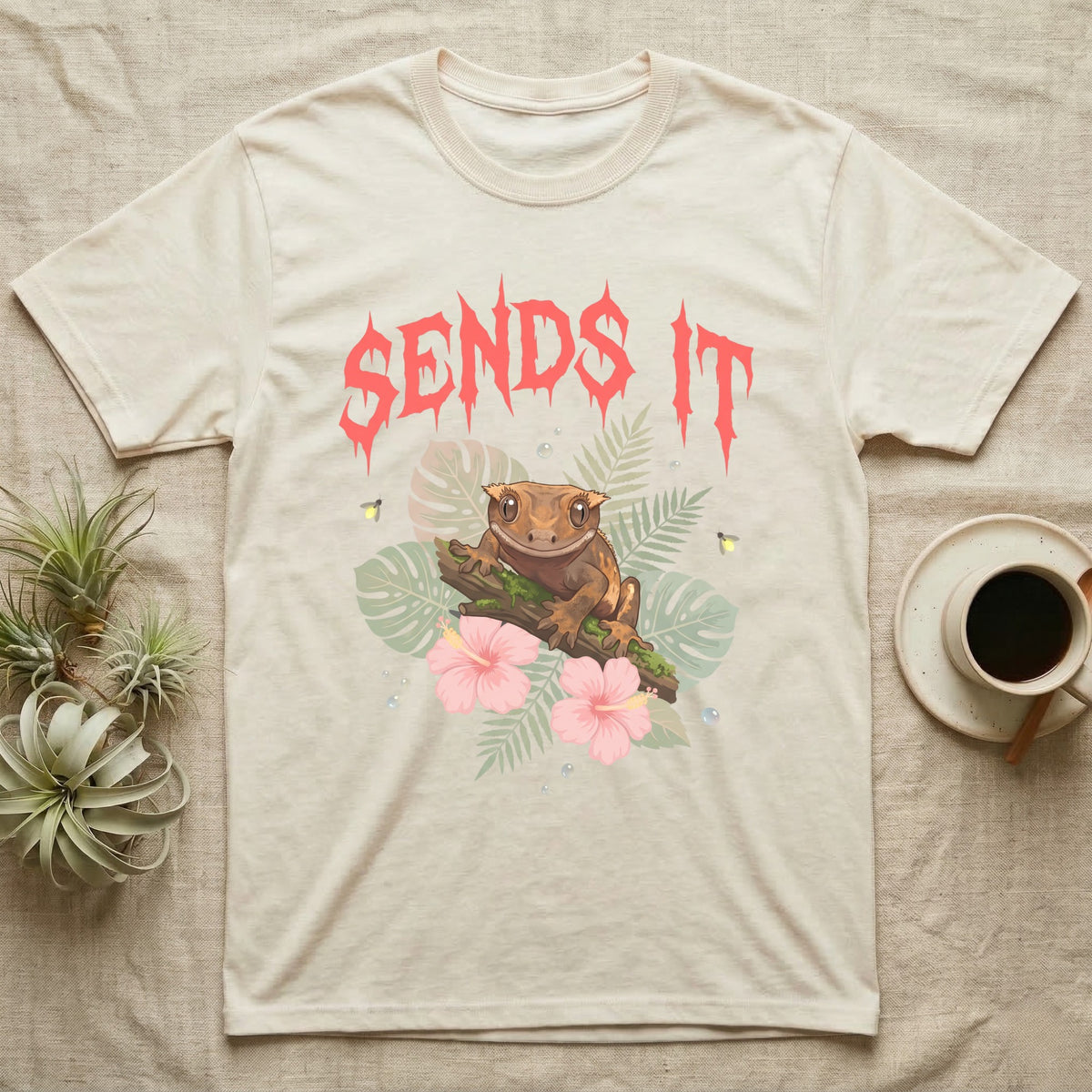 Crested Gecko Feral T-Shirt in Natural — Crested gecko on a mossy branch in a pastel jungle scene under a spiky coral metal wordmark reading SENDS IT.