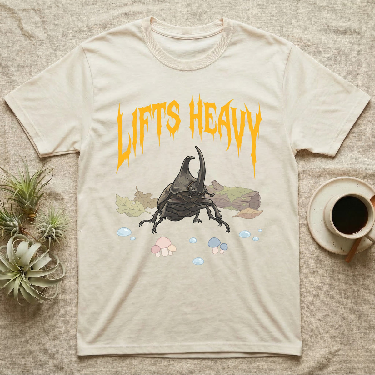 Rhino Beetle Feral T-Shirt in Natural — Horned rhinoceros beetle standing head-on below a dripping amber-gold metal "Lifts Heavy" wordmark