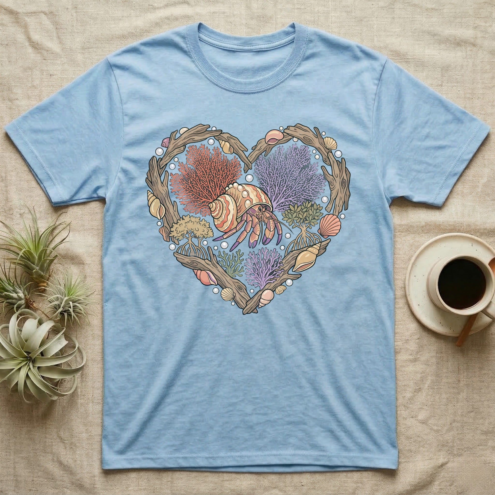 Light blue t-shirt with a heart-shaped design of shells and coral featuring a hermit crab.
