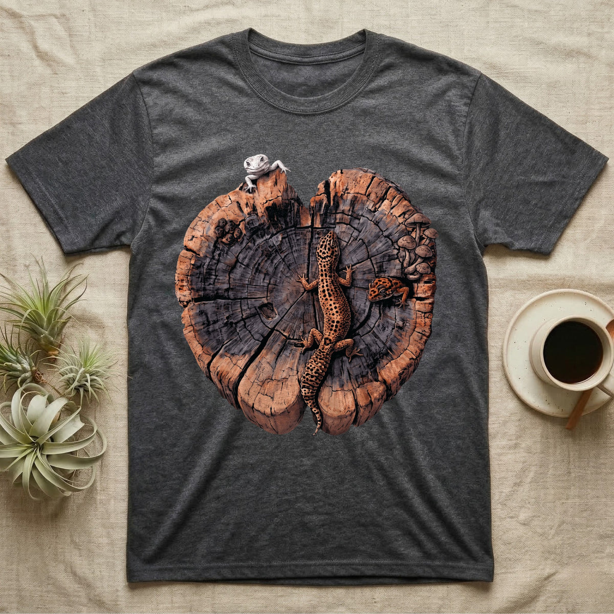 Leopard Gecko Stump Trio T-Shirt in Dark Heather — Three leopard geckos including a leucistic white morph on a cross-section log slab of amber growth rings with mushrooms, no on-shirt text.
