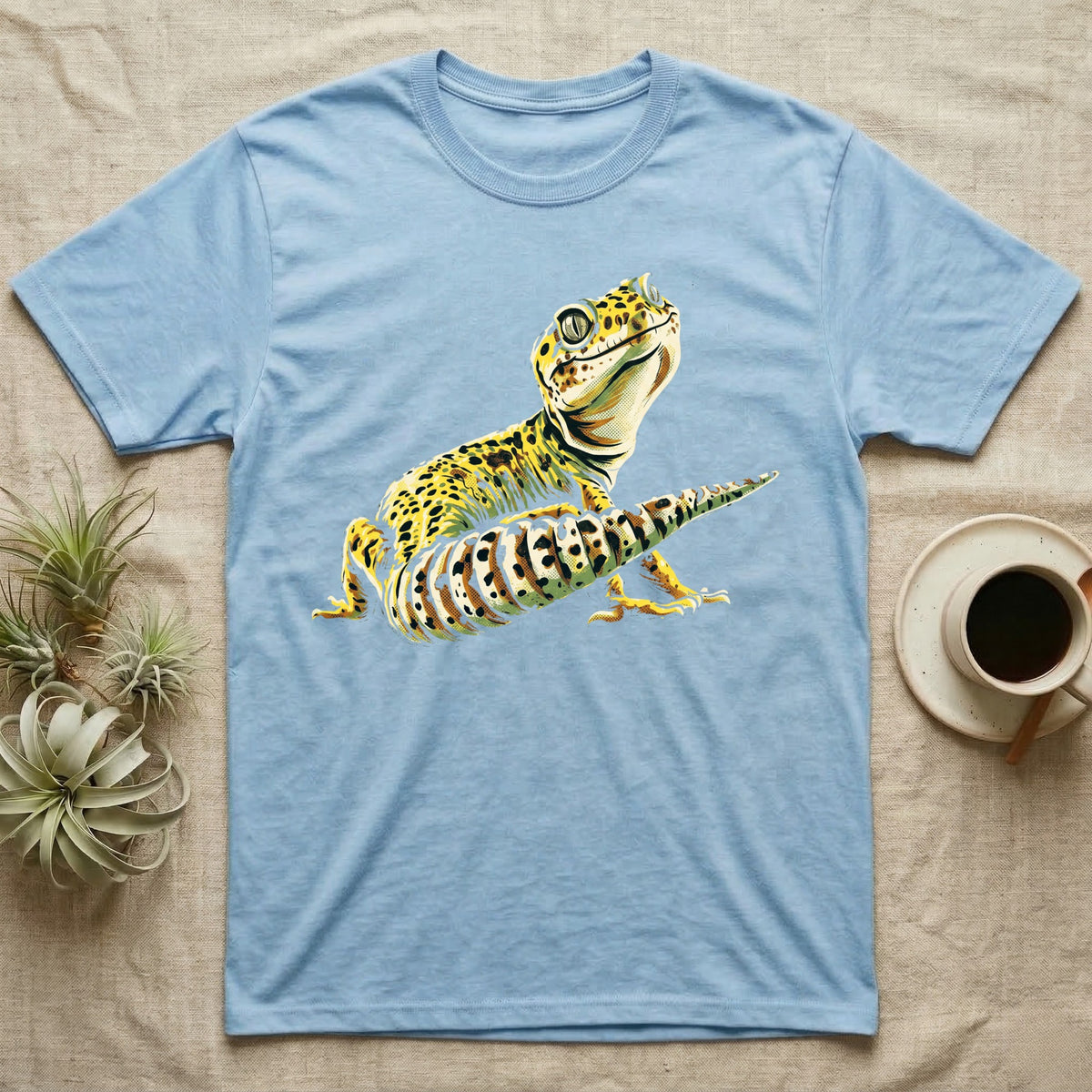 Illustration of a smiling leopard gecko with a plump curled spotted tail, bold vintage-comic ink outlines and halftone shading, graphic-only, no text. — shown on a Light Blue tee.