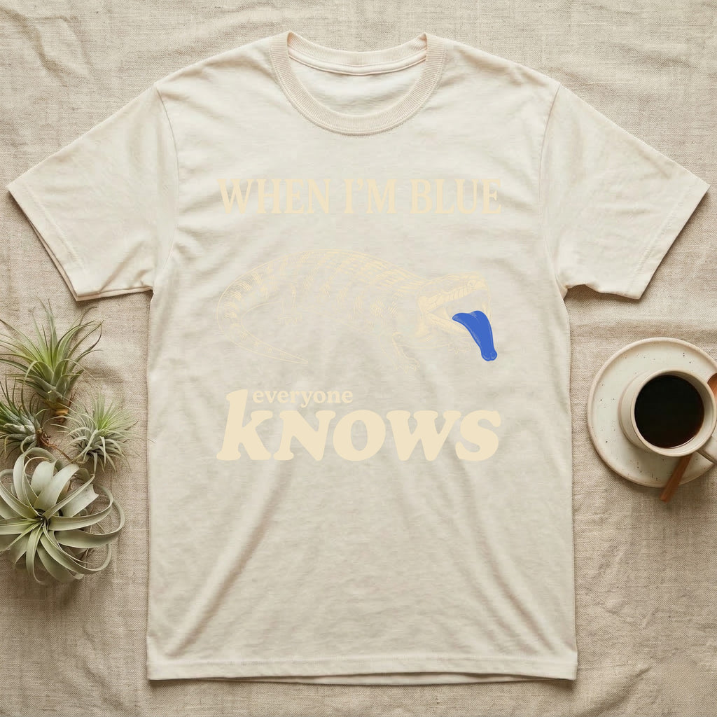 Blue-Tongue Skink Mood T-Shirt — Cream engraved blue-tongued skink on black flashing a cobalt blue tongue under the words WHEN I'M BLUE everyone KNOWS