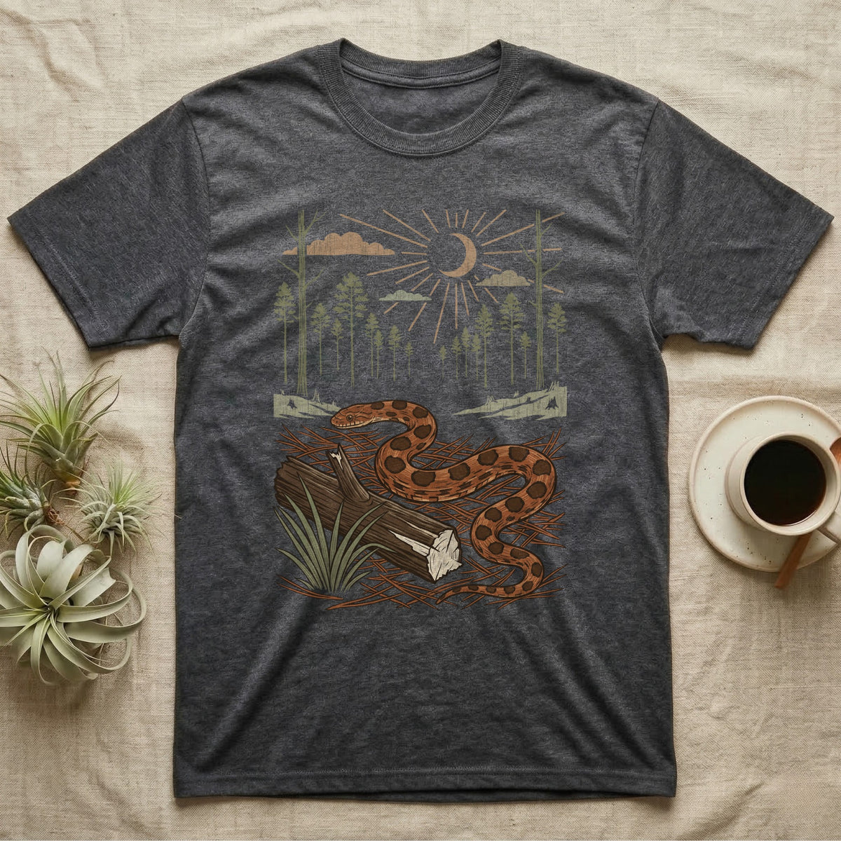 Corn Snake Home Range T-Shirt in Dark Heather — Woodcut-style illustration of a corn snake winding across pine straw beside a split log with pine trees behind, no on-shirt text.