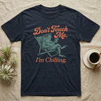 American Toad Deck Chair T-Shirt in Navy — Illustrated American toad reclining in a deck chair with sunglasses and a drink, coral script reading Don't Touch Me I'm Chilling.