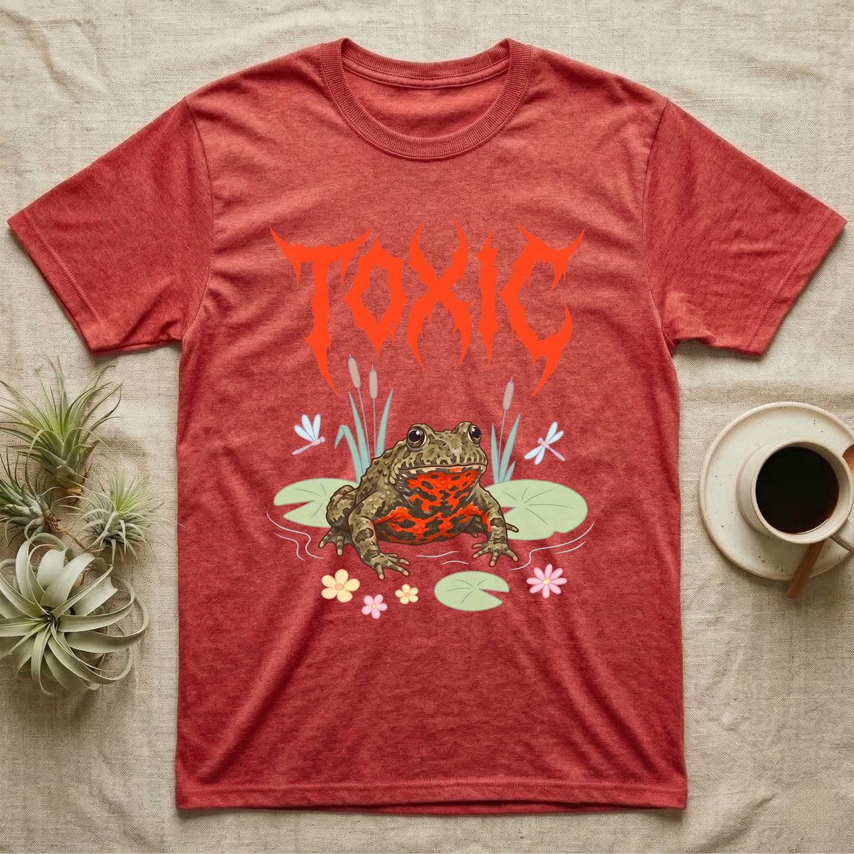 Oriental Fire-Bellied Toad Feral T-Shirt in Heather Red — Pastel fire-bellied toad with red-orange belly among lily pads and dragonflies, jagged metal wordmark "TOXIC" above.