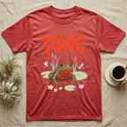 Oriental Fire-Bellied Toad Feral T-Shirt in Heather Red — Pastel fire-bellied toad with red-orange belly among lily pads and dragonflies, jagged metal wordmark "TOXIC" above.