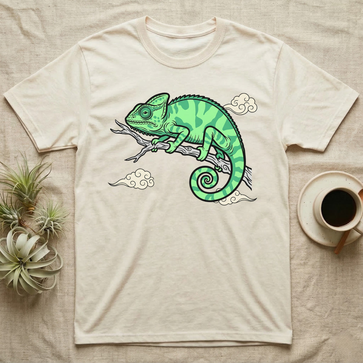 Cream t-shirt with green chameleon illustration and stylized clouds.