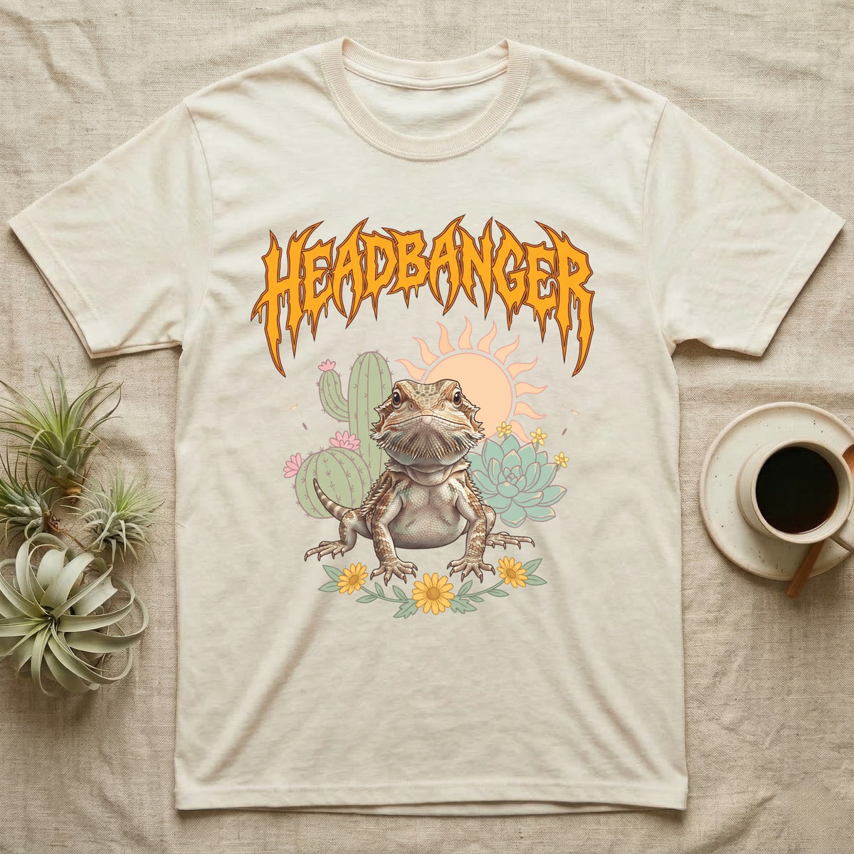 Central Bearded Dragon Feral T-Shirt in Natural — Baby bearded dragon in a pastel desert scene under a spiky amber metal wordmark reading HEADBANGER.