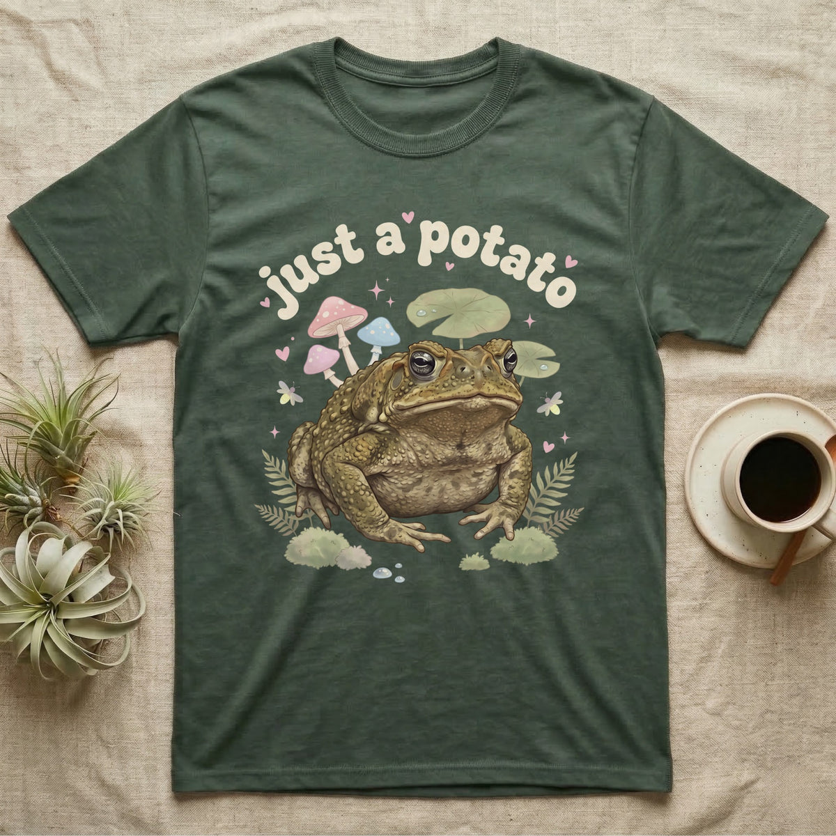 Cane Toad Baby T-Shirt in Military Green — Warty cane toad among pastel toadstools and lily pads under puffy cream bubble text "just a potato".