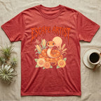 Corn Snake Feral T-Shirt in Heather Red — Orange corn snake coiled in a pastel cornfield scene under a spiky blood-orange metal wordmark reading ESCAPE ARTIST.