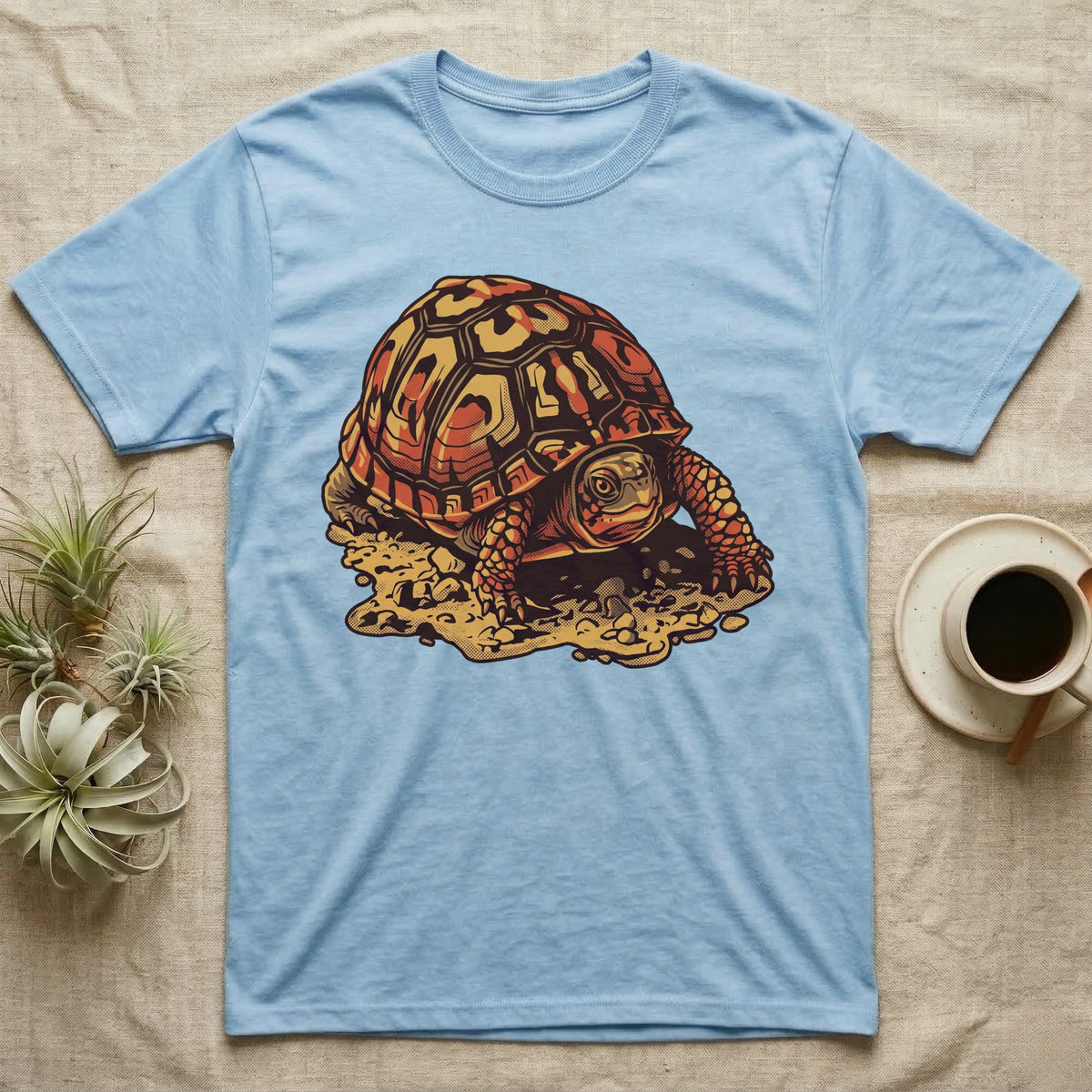 Vintage ink illustration of an Eastern box turtle crawling across sandy pebbles, high-domed shell shown in rust-red and amber, no on-shirt text. — shown on a Light Blue tee.