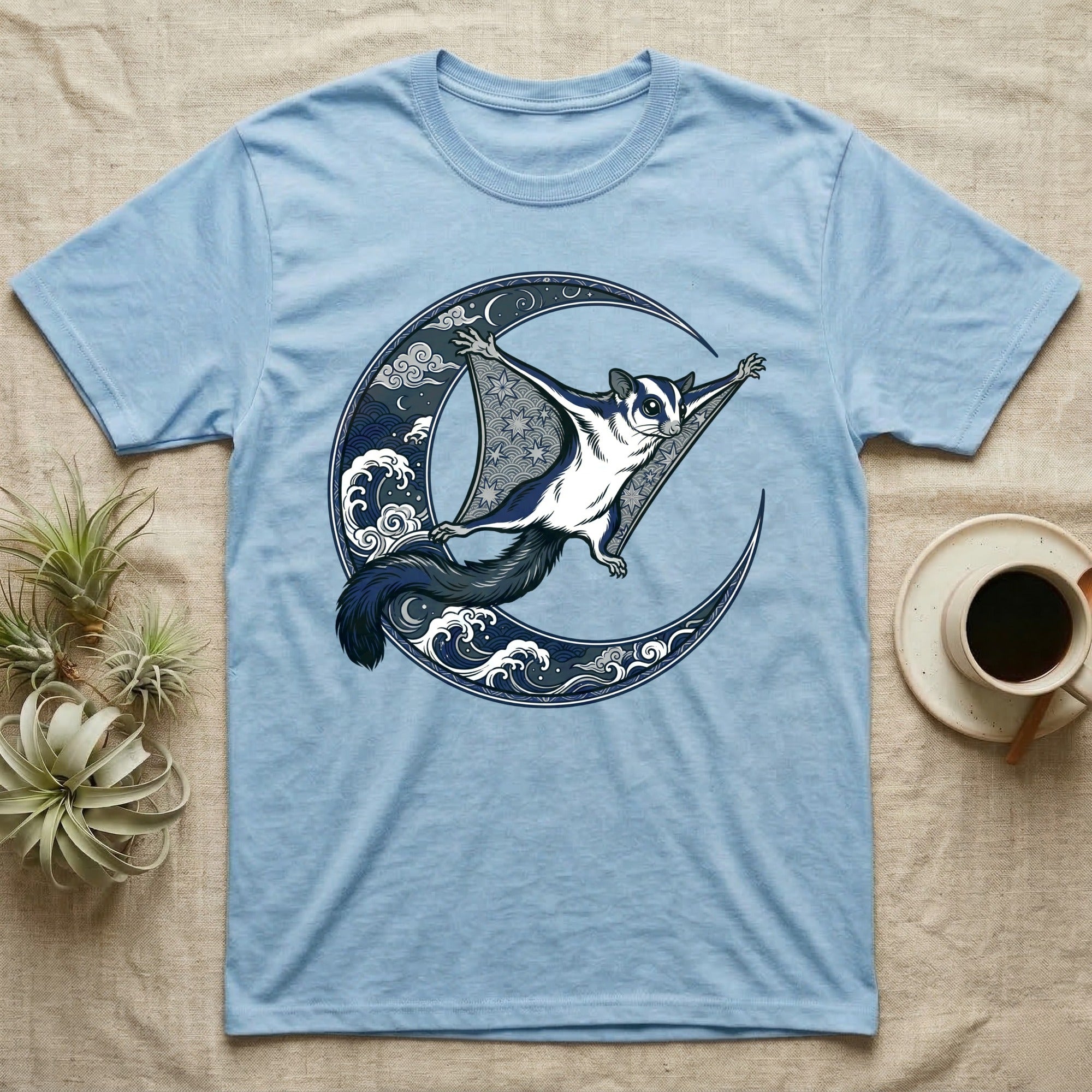 Light blue t-shirt with a sugar glider flying in a crescent moon with waves.