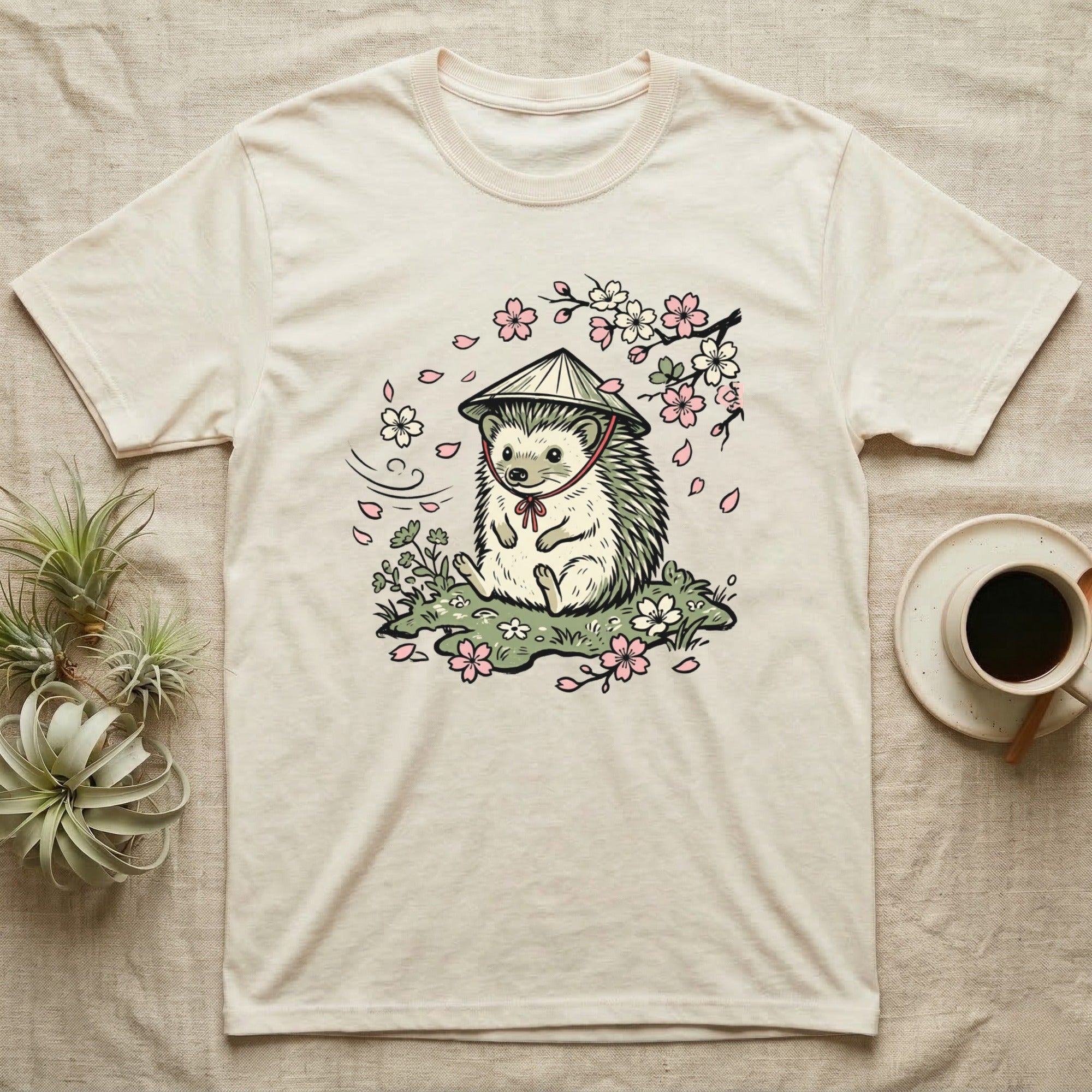 Cream t-shirt with a hedgehog wearing a straw hat under cherry blossoms.