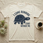 Red-Foot Tortoise Running T-Shirt in Natural — Navy silhouette of a red-footed tortoise walking under arched words I Come Running, beside Start Without Me