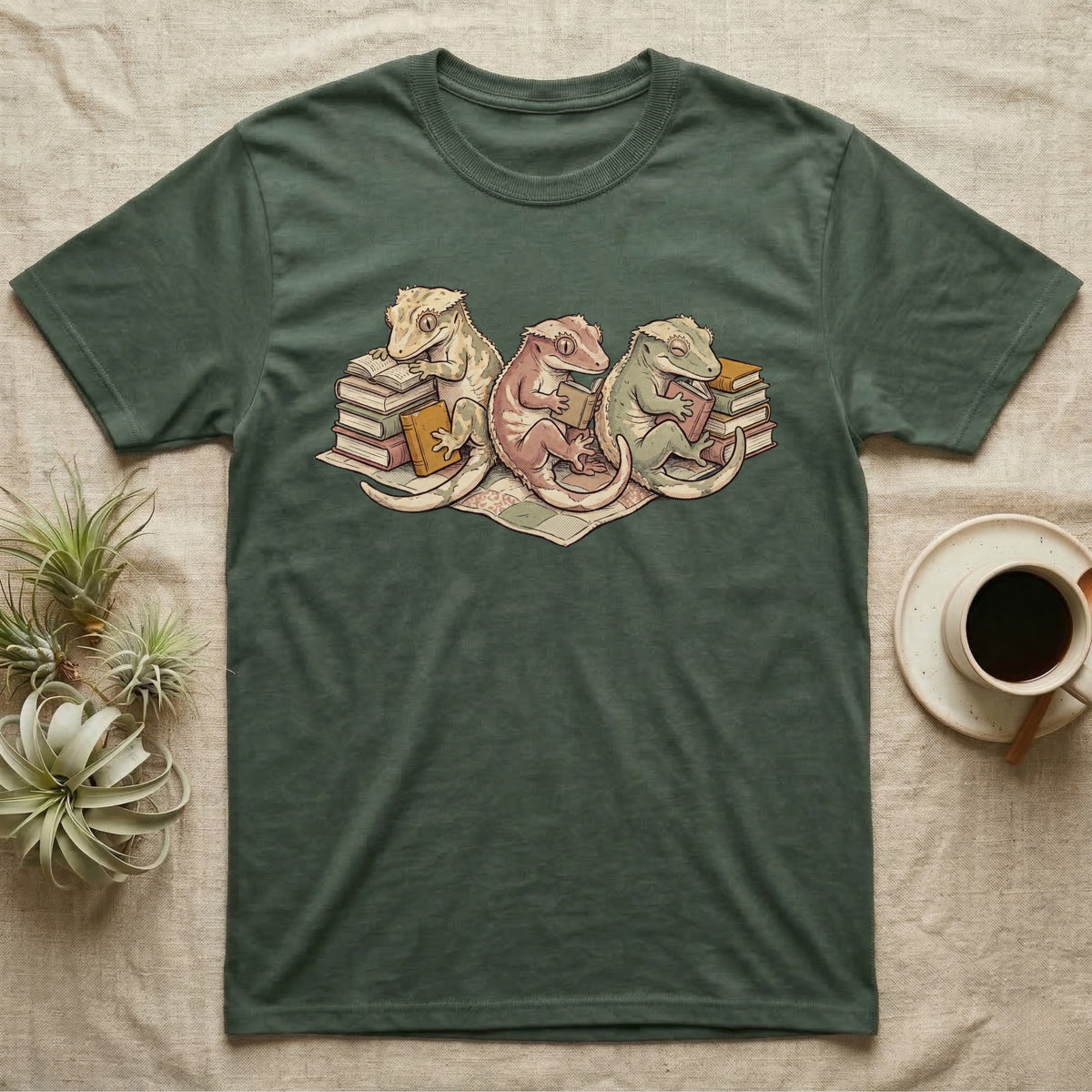 Gecko Book Club T-Shirt in Military Green — Warm storybook illustration of three crested geckos in a cozy reading row, each beside a tiny stack of books.