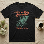 Poison Dart Frog Jumpsuit T-Shirt in Black — Illustrated green and black poison dart frog reclining in a beach chair with sunglasses and a cocktail, coral script asking what stylish frogs wear, answer jumpsuits.