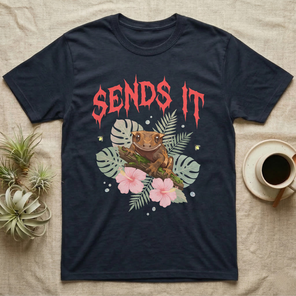 Crested Gecko Feral T-Shirt in Navy — Crested gecko on a mossy branch in a pastel jungle scene under a spiky coral metal wordmark reading SENDS IT.
