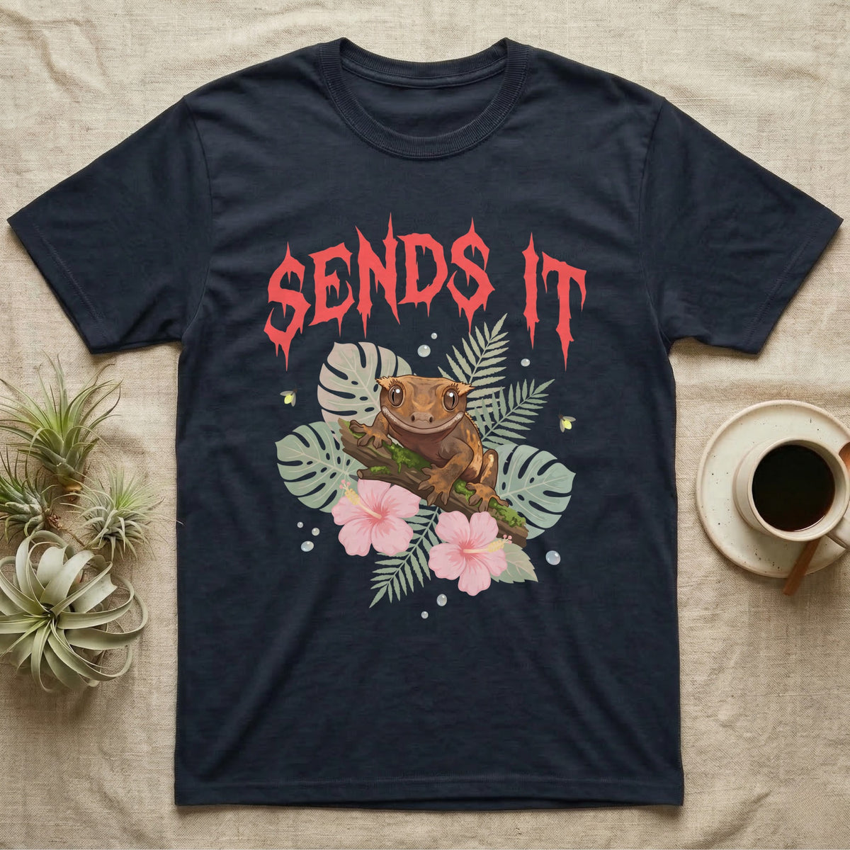 Crested Gecko Feral T-Shirt in Navy — Crested gecko on a mossy branch in a pastel jungle scene under a spiky coral metal wordmark reading SENDS IT.